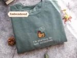 Sage green embroidered crewneck sweatshirt with brown pixel art sleepy chicken and I'm starting to feel exhausted text on rustic slate with pinecone and autumn leaves