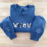 Folded indigo blue crewneck sweatshirt featuring four embroidered dogs and cats on chest with custom pet names Simon, Pito, Denali, and Gweny on sleeves