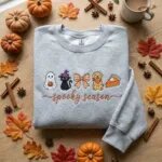 Ash grey sweatshirt embroidered with a cute ghost, witch cat, coquette bow, golden dog and pumpkin pie above "spooky season" in cursive