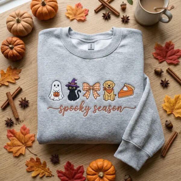 Ash grey sweatshirt embroidered with a cute ghost, witch cat, coquette bow, golden dog and pumpkin pie above "spooky season" in cursive