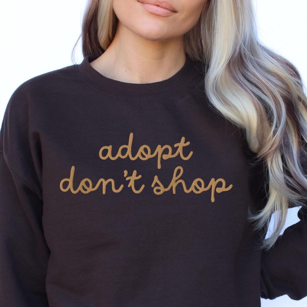 Adopt Don't Shop Sweatshirt - worn Woman in a dark crewneck sweatshirt embroidered with adopt don't shop in a gold cursive script across the chest