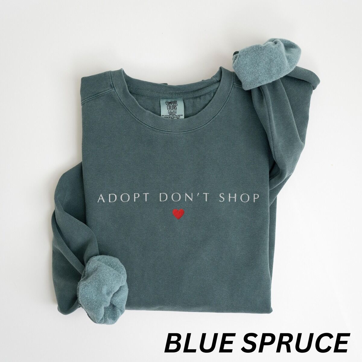 Adopt Don't Shop Sweatshirt – Blue Spruce Blue Spruce crewneck sweatshirt laid flat on white, embroidered with ADOPT DON'T SHOP in light spaced capitals and a red heart