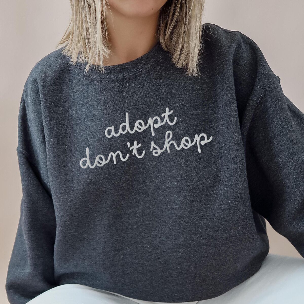 Adopt Don't Shop Sweatshirt - Dark Heather Woman in a Dark Heather crewneck sweatshirt embroidered with adopt don't shop in a light grey cursive script