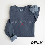 Denim adopt don't shop sweatshirt laid flat on white with rolled cuffs, embroidered with ADOPT DON'T SHOP in white spaced capitals and a small red heart