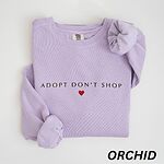 Orchid crewneck sweatshirt laid flat on white, embroidered with ADOPT DON'T SHOP in dark capitals and a small red heart