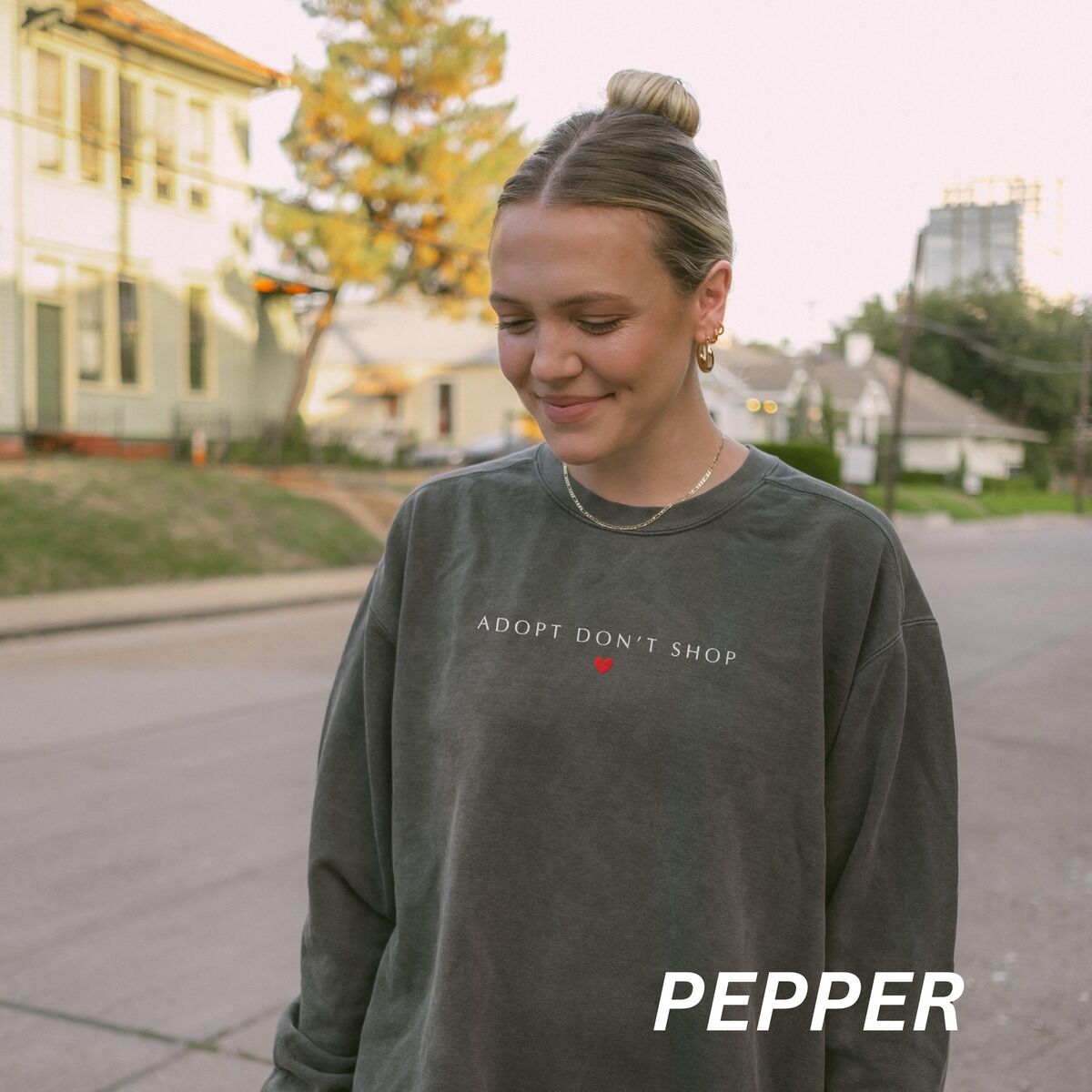 Adopt Don't Shop Sweatshirt – Pepper Woman on a city street in a Pepper crewneck sweatshirt embroidered with ADOPT DON'T SHOP in light capitals and a small red heart