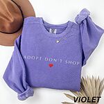 Violet crewneck sweatshirt laid flat with a felt hat and dried palm leaves, embroidered with ADOPT DON'T SHOP in light capitals and a red heart