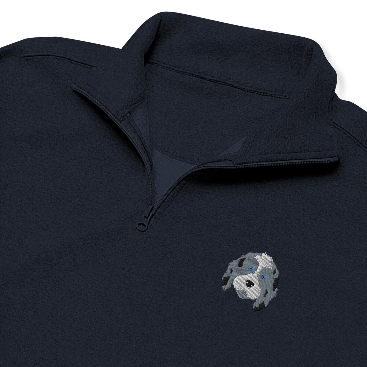 Aussiedoodle Quarter Zip - Navy close-up Close-up of a Navy quarter zip collar and chest, embroidered with a blue merle aussiedoodle face with a white blaze and blue eyes on the left chest
