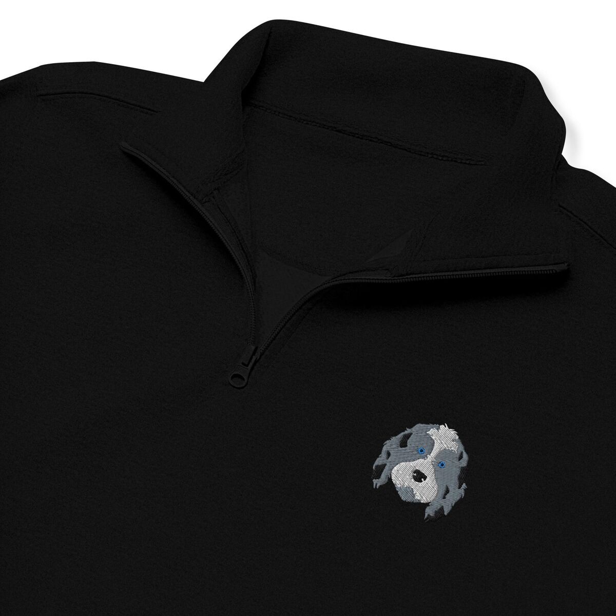 Aussiedoodle Quarter Zip – Black Close-up of a Black quarter zip collar and chest, embroidered with a blue merle aussiedoodle face with a white blaze and blue eyes on the left chest