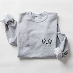 Sport Grey crewneck sweatshirt laid flat on a white background, embroidered with a fluffy grey aussiedoodle face with spotted merle ears and blue eyes on the left chest