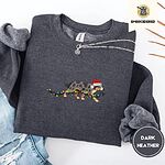 Dark Heather crewneck sweatshirt folded with ripped jeans and a silver chain necklace, embroidered with a blue merle Australian Shepherd in a Santa hat trotting with a string of Christmas lights in its mouth