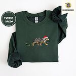 Forest Green crewneck sweatshirt folded on a white background, embroidered with a blue merle Australian Shepherd in a Santa hat trotting with a string of Christmas lights in its mouth