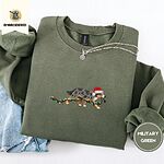 Military Green crewneck sweatshirt folded with light jeans and a silver chain necklace, embroidered with a blue merle Australian Shepherd in a Santa hat trotting with a string of Christmas lights in its mouth