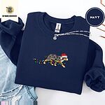 Navy crewneck sweatshirt folded with ripped jeans and a silver chain necklace, embroidered with a blue merle Australian Shepherd in a Santa hat trotting with a string of Christmas lights in its mouth