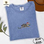 Blue Jean Comfort Colors T-shirt embroidered with a blue merle Australian Shepherd in a Santa hat trotting with a string of Christmas lights in its mouth