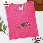 Crunchberry Comfort Colors T-shirt embroidered with a blue merle Australian Shepherd in a Santa hat trotting with a string of Christmas lights in its mouth
