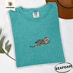 Seafoam Comfort Colors T-shirt embroidered with a blue merle Australian Shepherd in a Santa hat trotting with a string of Christmas lights in its mouth