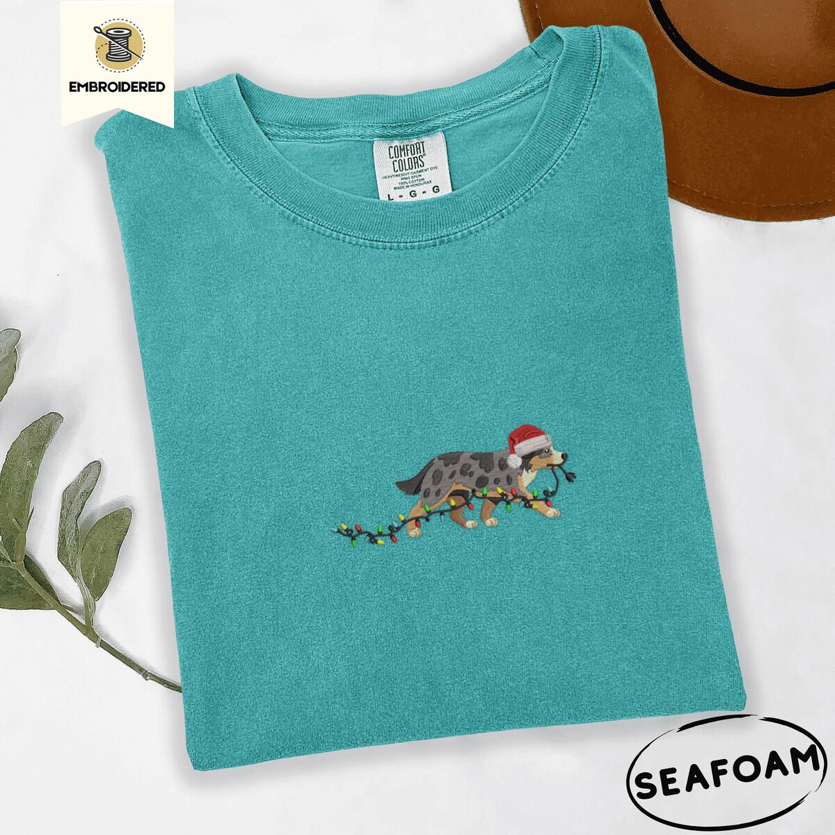 Australian Shepherd Santa Hat Shirt – Seafoam Seafoam Comfort Colors T-shirt embroidered with a blue merle Australian Shepherd in a Santa hat trotting with a string of Christmas lights in its mouth