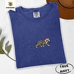 True Navy Comfort Colors T-shirt embroidered with a blue merle Australian Shepherd in a Santa hat trotting with a string of Christmas lights in its mouth