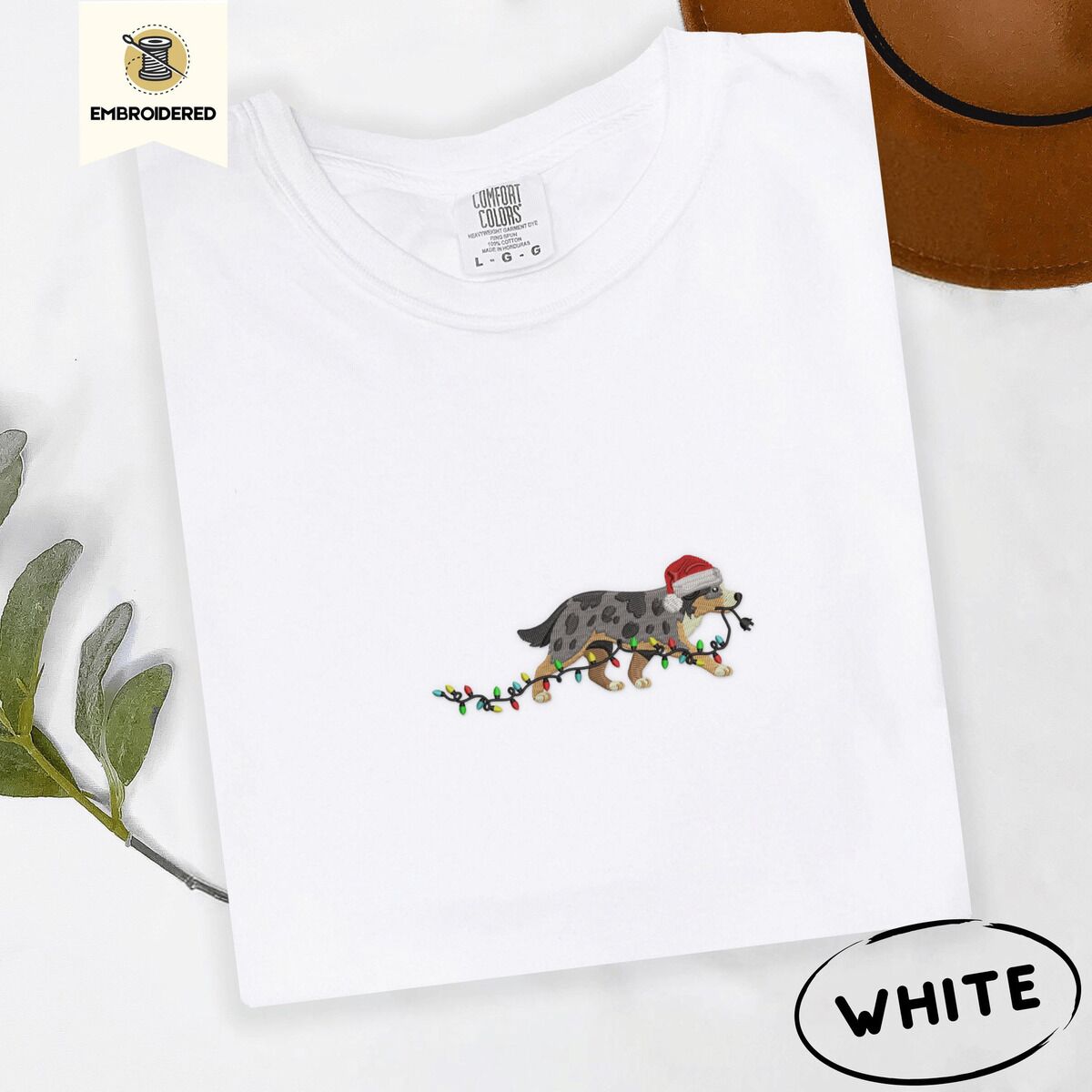 Australian Shepherd Santa Hat Shirt – White White Comfort Colors T-shirt embroidered with a blue merle Australian Shepherd in a Santa hat trotting with a string of Christmas lights in its mouth