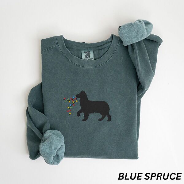 Blue Spruce crewneck sweatshirt laid flat with rolled cuffs, embroidered with a black Australian shepherd silhouette carrying a string of Christmas lights