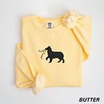 Butter crewneck sweatshirt laid flat with rolled cuffs, embroidered with a black Australian shepherd silhouette carrying a string of Christmas lights