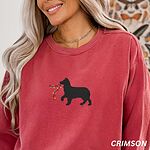 Woman with a gold necklace in a Crimson crewneck sweatshirt embroidered with a black Australian shepherd silhouette carrying a string of Christmas lights