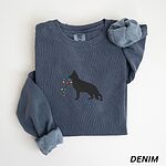 Denim crewneck sweatshirt laid flat with rolled cuffs, embroidered with a black Australian shepherd silhouette carrying a string of Christmas lights
