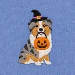 Close-up of the embroidered Australian Shepherd in a witch hat with a jack-o'-lantern candy bucket