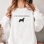 Woman in a White crewneck sweatshirt embroidered with In My Berner Mom Era and a standing Bernese mountain dog across the chest