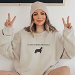 Woman in a beanie making peace signs in a Sand Berner mom sweatshirt embroidered with In My Berner Mom Era and a tricolor Berner