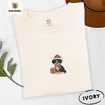 Ivory Comfort Colors T-shirt embroidered with a tricolor Bernese mountain dog puppy in a Santa hat and knit scarf sitting beside a wrapped gift