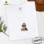 White Comfort Colors T-shirt embroidered with a tricolor Bernese mountain dog puppy in a Santa hat and knit scarf sitting beside a wrapped gift