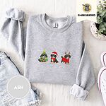 Ash crewneck sweatshirt folded with denim shorts, white sneakers and a potted plant, embroidered with three Bernese mountain dog puppies in a Christmas tree costume, a Santa hat with a red scarf and reindeer antlers with a red sweater