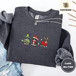 Dark Heather crewneck sweatshirt folded with ripped jeans and a silver chain necklace, embroidered with three Bernese mountain dog puppies in a Christmas tree costume, a Santa hat with a red scarf and reindeer antlers with a red sweater