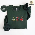 Forest Green crewneck sweatshirt folded on a white background, embroidered with three Bernese mountain dog puppies in a Christmas tree costume, a Santa hat with a red scarf and reindeer antlers with a red sweater