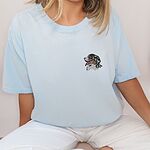 Woman sitting in an Ice Blue T-shirt embroidered with a small Bernese mountain dog head in profile on the left chest