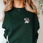 Woman in a Forest Green crewneck sweatshirt embroidered with a tricolor Bernese mountain dog head on the left chest