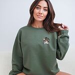 Woman in a Military Green crewneck sweatshirt embroidered with a small Berner head with its tongue out on the left chest