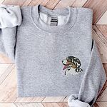 Sport Grey crewneck sweatshirt laid flat on herringbone wood, embroidered with a tricolor Berner head with its pink tongue out on the left chest