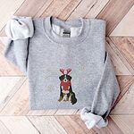 Sport Grey crewneck sweatshirt laid flat on a chevron wood floor, embroidered with a sitting tricolor Bernese mountain dog in red reindeer antlers and a red knit scarf, framed by snowflakes