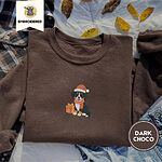 Dark Chocolate crewneck sweatshirt on a plaid flannel shirt with yellow autumn leaves and denim shorts, embroidered with a tricolor Bernese mountain dog puppy in a Santa hat and knit scarf sitting beside a wrapped gift