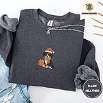 Dark Heather crewneck sweatshirt folded with ripped jeans and a silver chain necklace, embroidered with a tricolor Bernese mountain dog puppy in a Santa hat and knit scarf sitting beside a wrapped gift