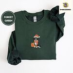 Forest Green crewneck sweatshirt folded on a white background, embroidered with a tricolor Bernese mountain dog puppy in a Santa hat and knit scarf sitting beside a wrapped gift