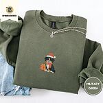 Military Green crewneck sweatshirt folded with light jeans and a silver chain necklace, embroidered with a tricolor Bernese mountain dog puppy in a Santa hat and knit scarf sitting beside a wrapped gift