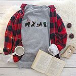 Grey crewneck sweatshirt laid flat with a red plaid flannel shirt, a mug and an open book, embroidered with four black Bernese mountain dog silhouettes in antlers, a Santa hat, a striped scarf and a green bow under a gold star