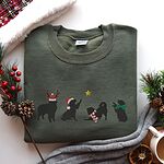 Military Green crewneck sweatshirt laid flat with pine cones and red berries, embroidered with four black Bernese mountain dog silhouettes in antlers, a Santa hat, a striped scarf and a green bow under a gold star
