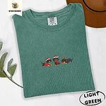 Light Green Comfort Colors T-shirt embroidered with three black and tan dachshunds in Santa hats, a red sweater, a red scarf and reindeer antlers