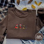 Dark Chocolate crewneck sweatshirt on a plaid flannel shirt with yellow autumn leaves and denim shorts, embroidered with three black and tan dachshunds in Santa hats, a red scarf and reindeer antlers across the chest