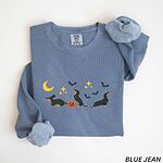 Blue Jean crewneck sweatshirt laid flat on white, embroidered with three black and tan dachshunds playing under a yellow crescent moon, gold stars and flying bats beside a small jack-o'-lantern